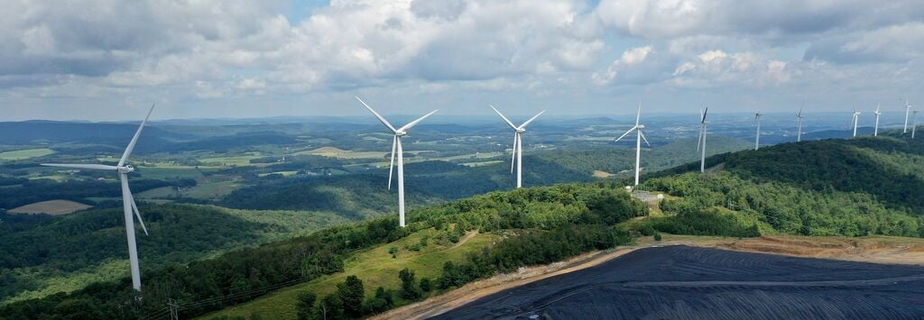 Wind turbines generating renewable energy on a reclaimed mining landscape surrounded by rolling green hills under a partly cloudy sky.